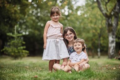 Trois enfants souriants posent ensemble dans un jardin verdoyant.