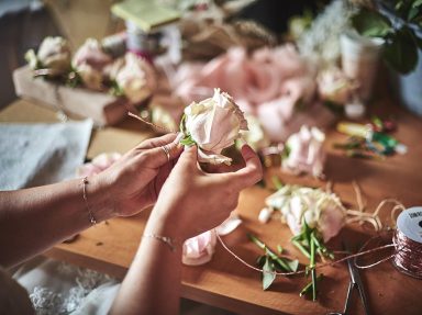 Des mains assemblent des fleurs sur une table, entourées de matériel de décoration.