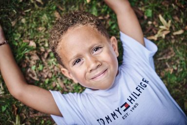 Un garçon souriant allongé sur l'herbe, portant un t-shirt blanc avec un logo.