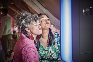 Deux femmes posent joyeusement, l'une avec des boucles grises et l'autre en robe colorée.