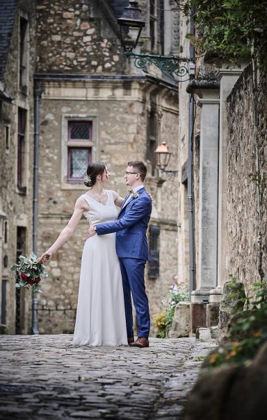 Mariage d'un couple dans une ruelle historique, avec des murs en pierre et des fleurs.