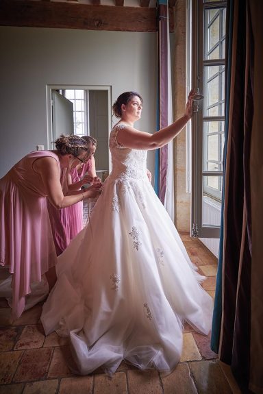 Une mariée ajuste sa robe pendant qu'une demoiselle d'honneur l'aide.