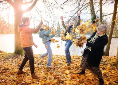 Groupe de personnes joyeuses lançant des feuilles d'automne près d'un lac.