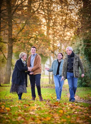 Quatre personnes marchent ensemble dans un parc en automne, entourées de feuilles tombées.